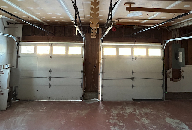 Old white garage doors in Point Pleasant NJ with visible drafts and snow buildup in front of the garage during winter