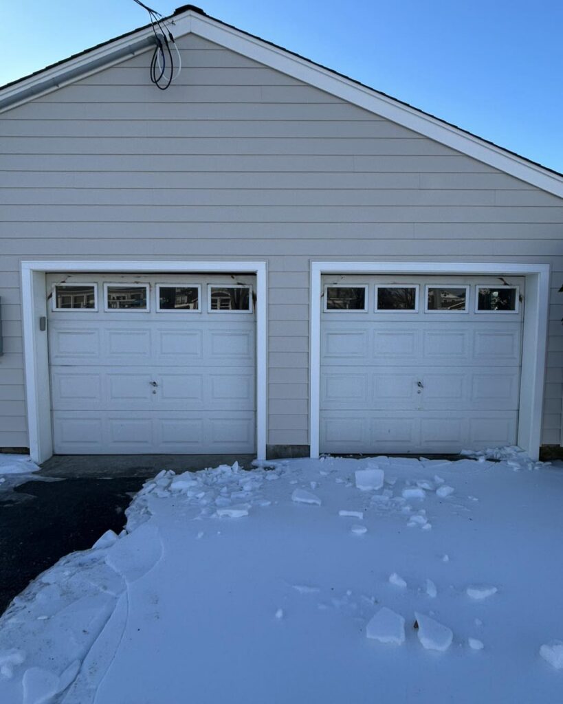 Old white garage doors in Point Pleasant NJ with visible drafts and snow buildup in front of the garage during winter