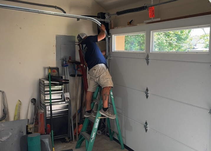 Surfside Garage Doors technician on a ladder performing garage door track realignment inside a residential garage in Ocean County, NJ.